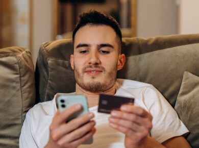man laid back on a couch holding a smartphone and card